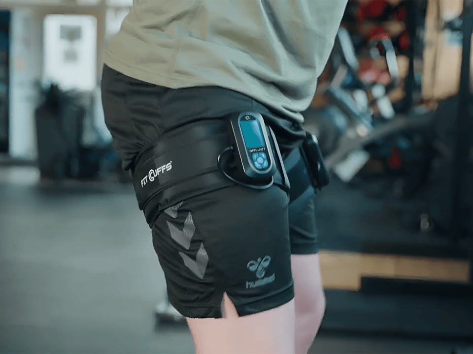 Fit Cuffs BFR Unit V1.1 connected to leg cuffs on both legs for low-load squats during blood flow restriction (BFR) training